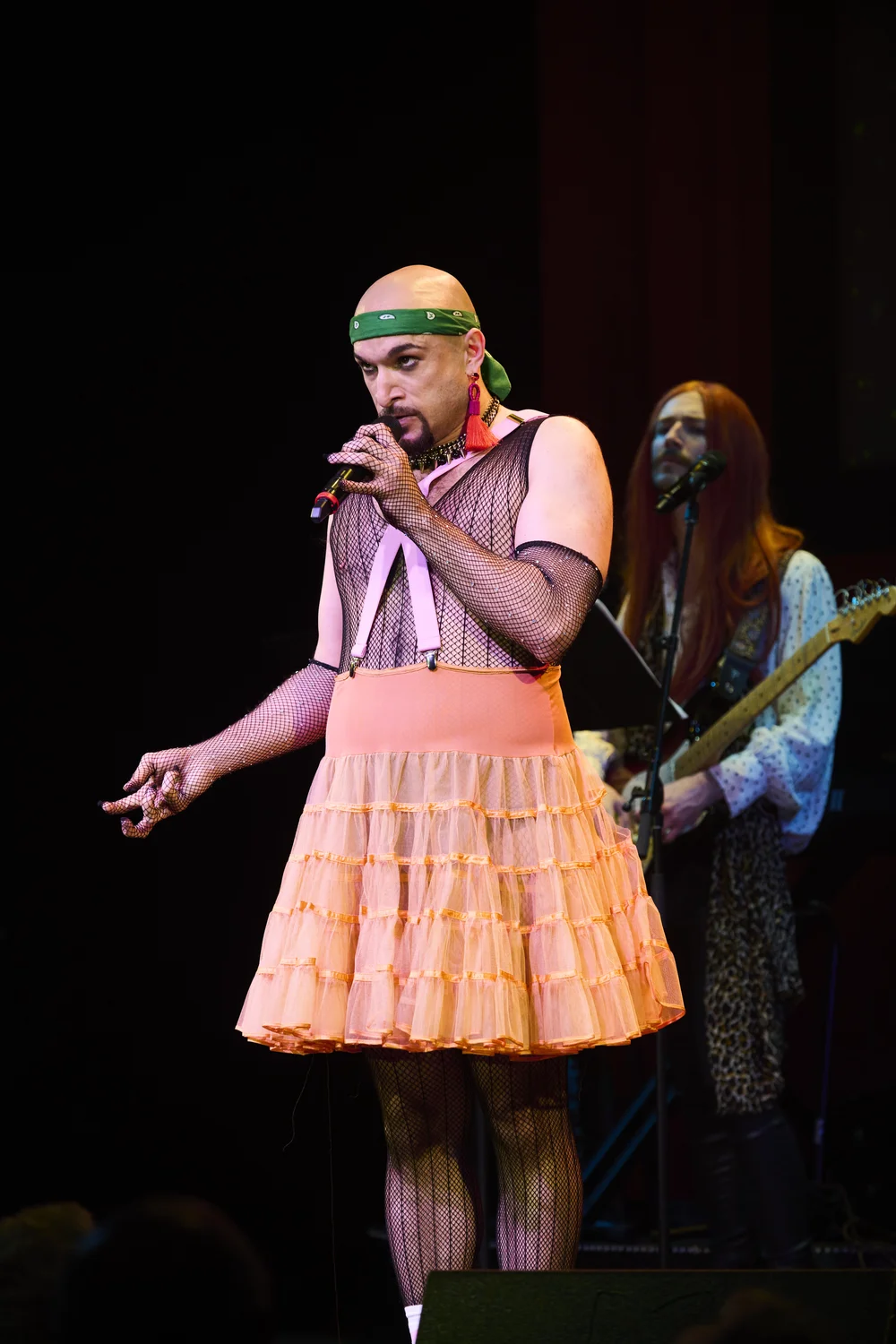 Jerreme Rodriguez performing with a microphone in an orange skirt at The Bash at City Theatre