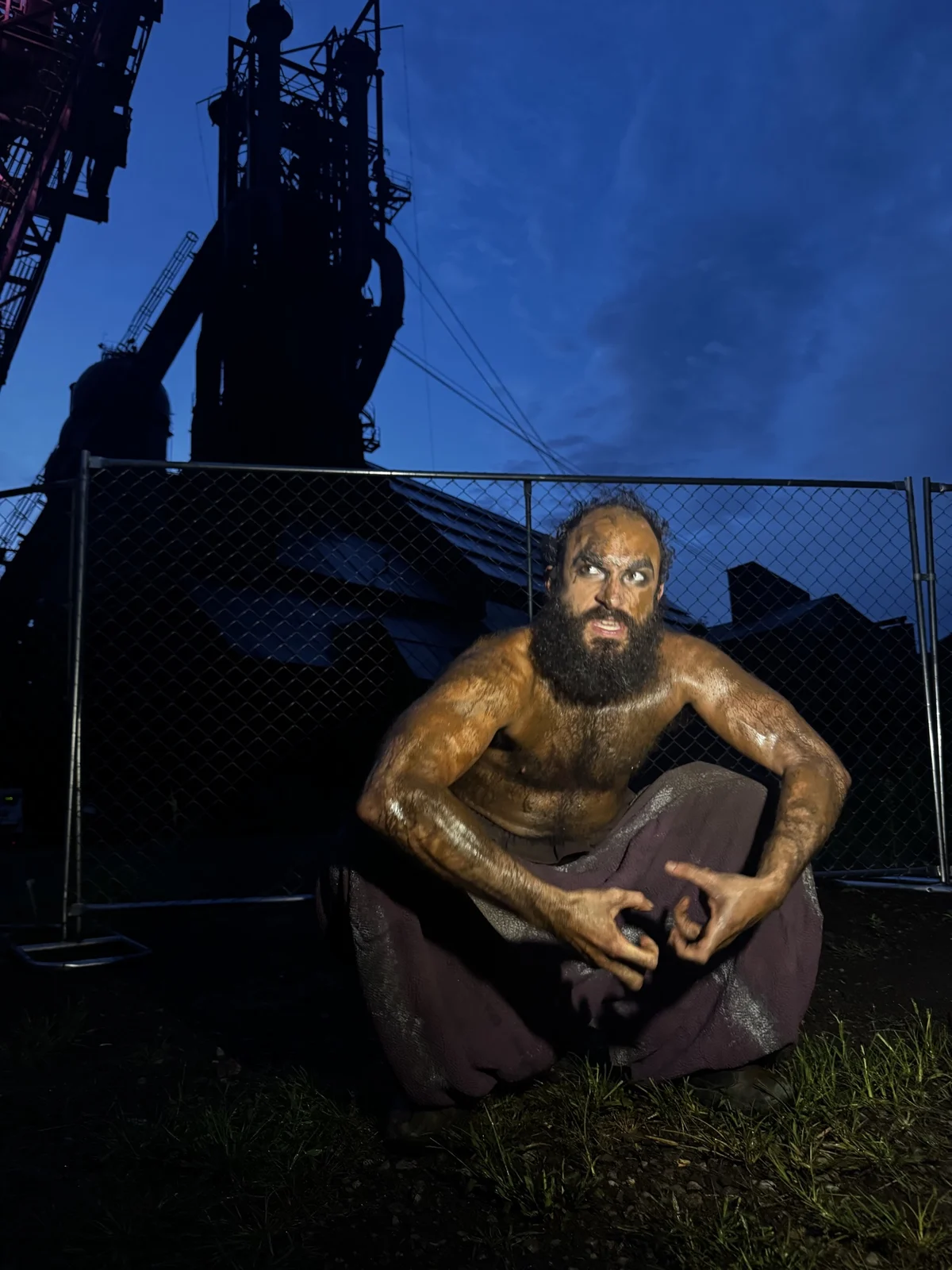 Jerreme Rodriguez as Caliban crouching beneath the industrial structures at Carrie Blast Furnaces
