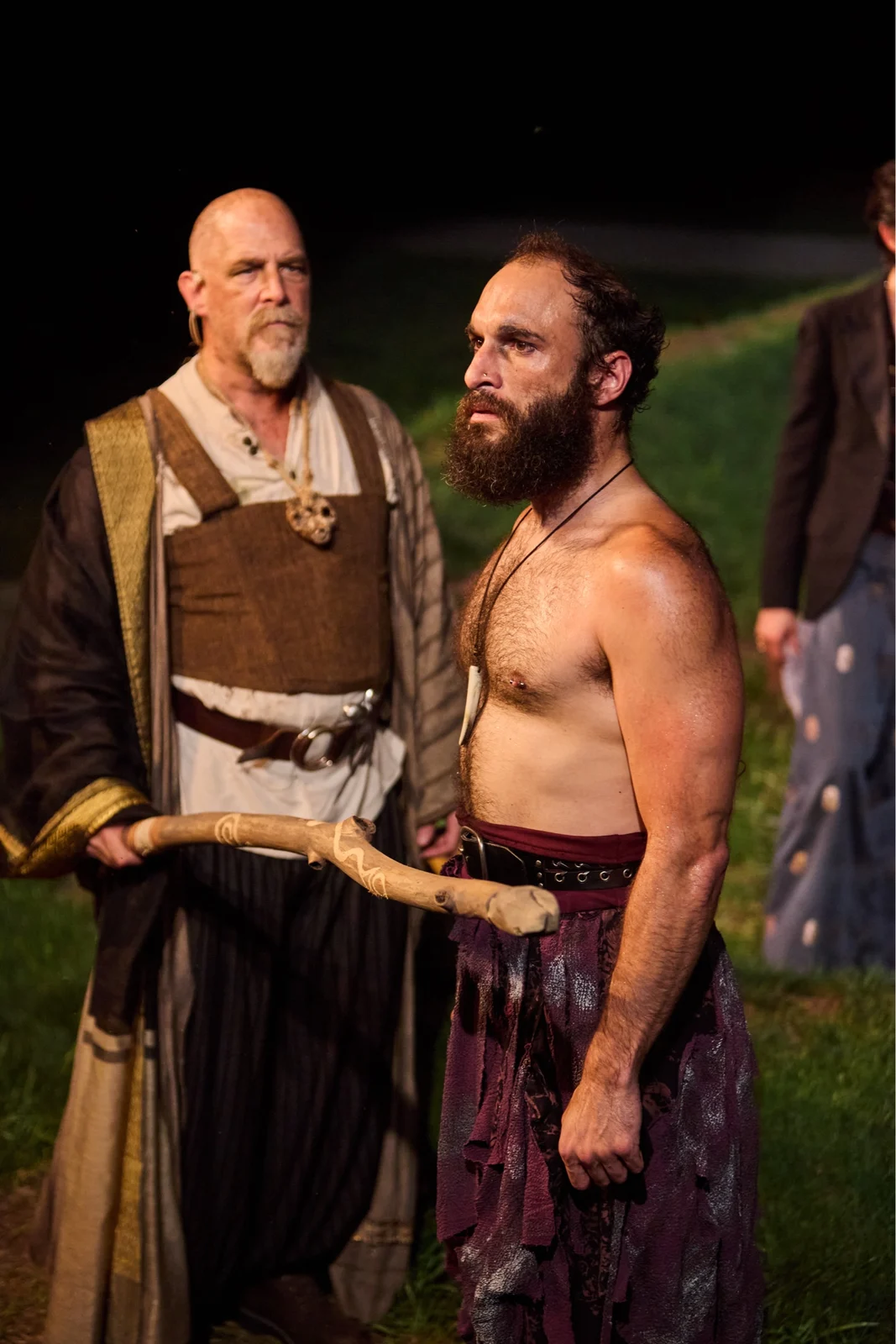 Caliban in a tense scene beside a performer holding a wooden staff in The Tempest