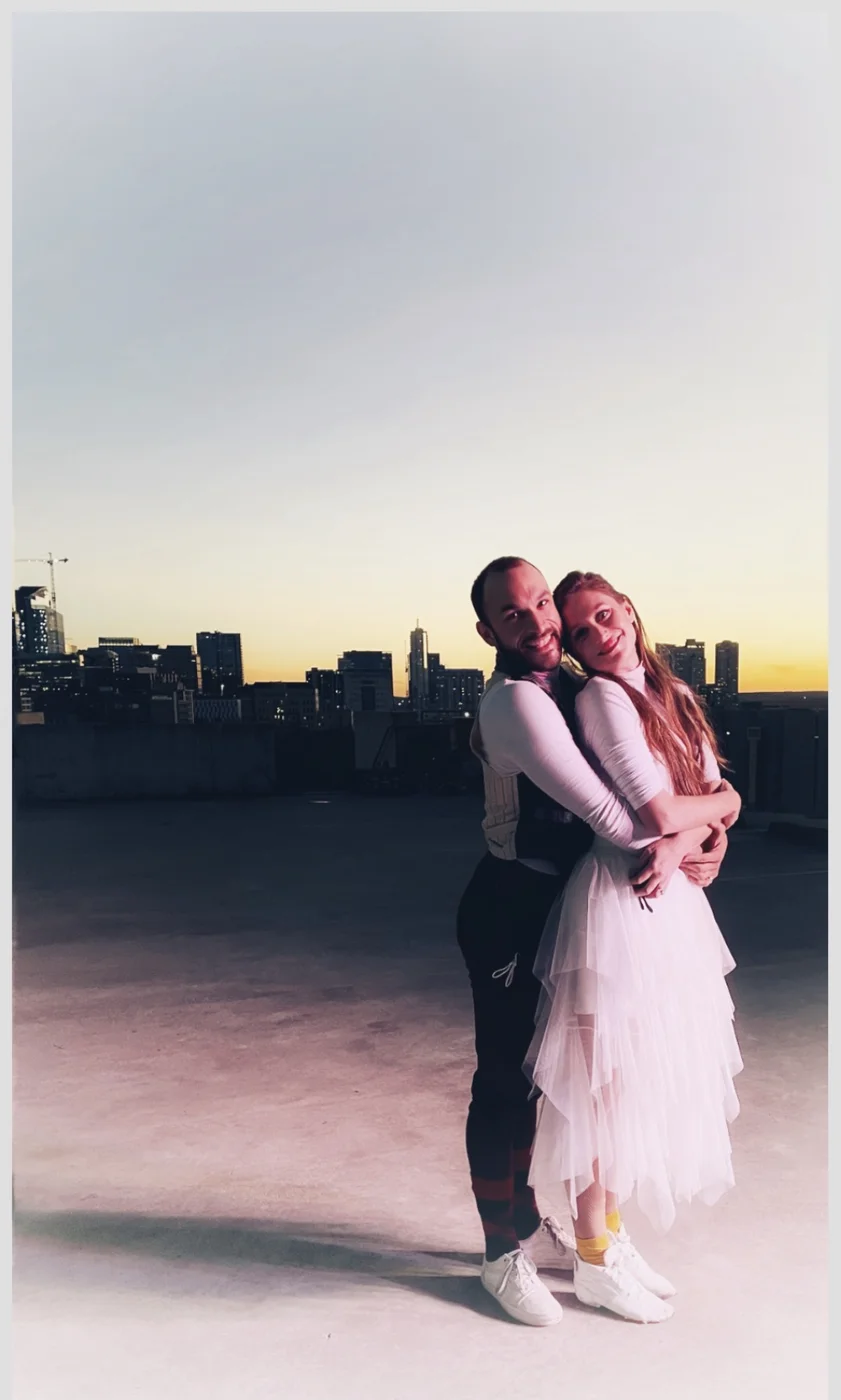 Two Watchmaker performers embracing outdoors against the skyline at sunset